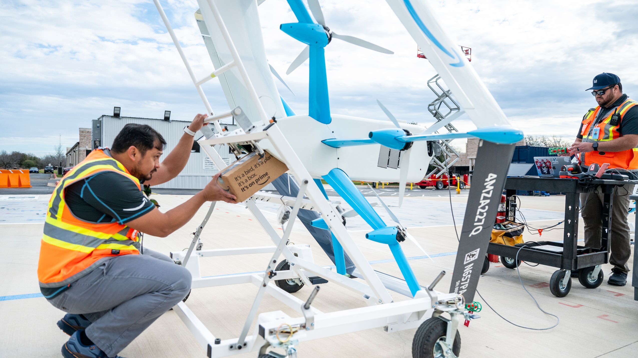 An image of two employees standing on a launch pad helping monitor and operate a drone that is taking flight.