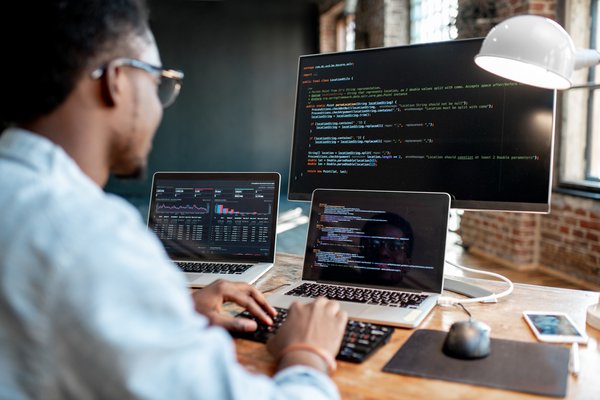 Software engineer typing on laptop with multiple screens in front of him.